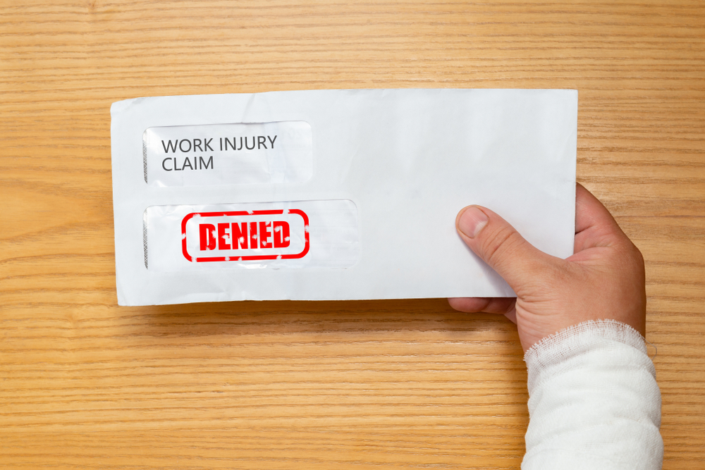 wrapped hand holding an envelope with a work injury claim application inside stamped with denied