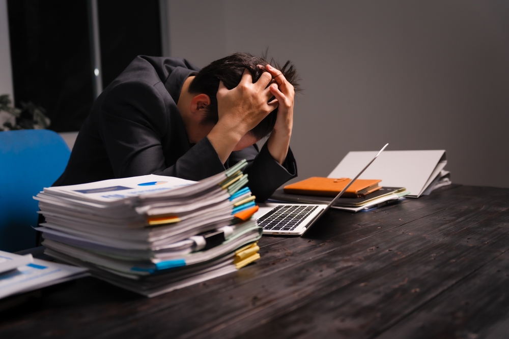 A stressed young Asian man in a formal suit works late at night at his desk